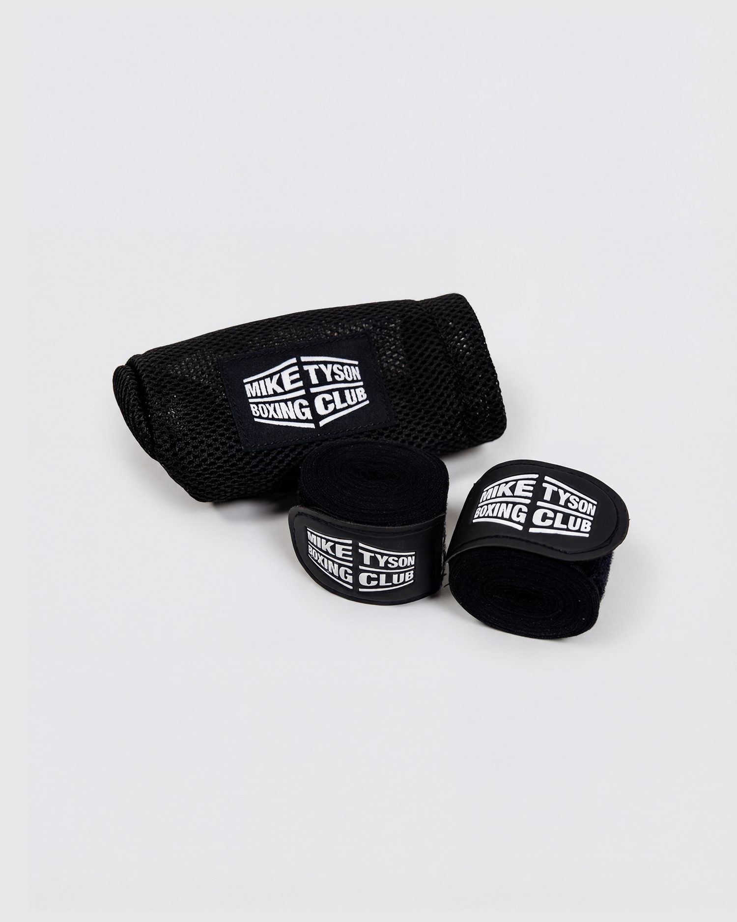Black boxing hand wraps with the Mike Tyson Boxing Club logo in white on the wrap closure. Black mesh laundry bag is in the background, also featuring the white logo.