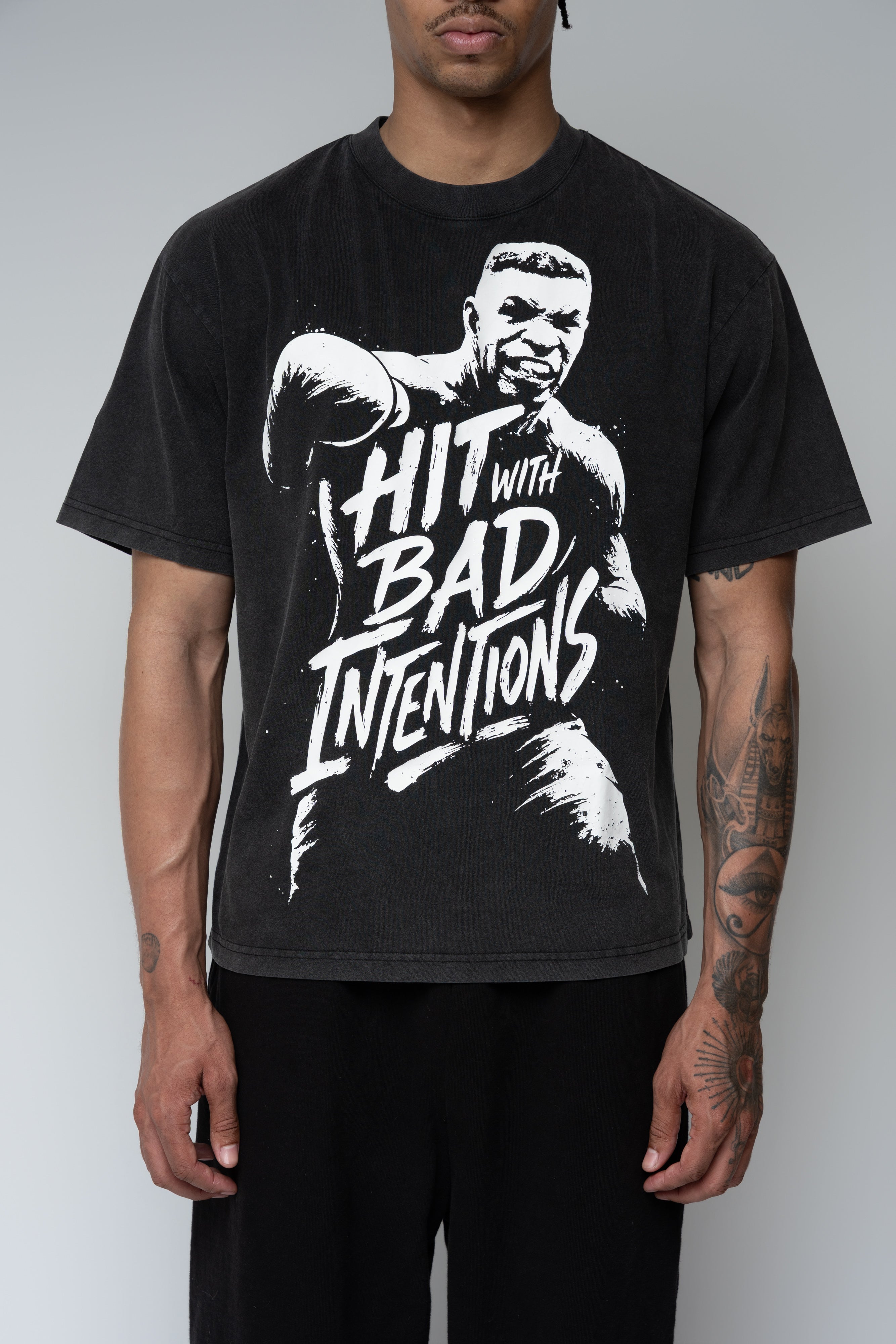 Model wearing a black T-shirt with a black and white image of Mike Tyson punching towards the viewer, with text over his torso that says "Hit with Bad Intentions" on the front.