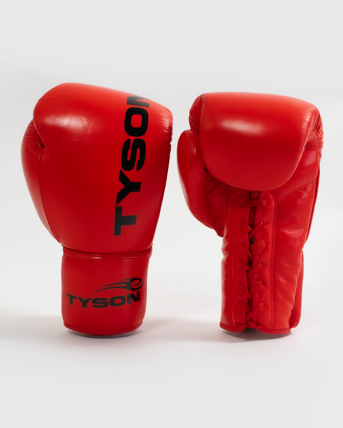 Red boxing gloves. Black text saying "Tyson" runs vertically towards the fingers on the back of the gloves, while the Tyson Pro logo is on the wrist. The palm side of the glove features laces.