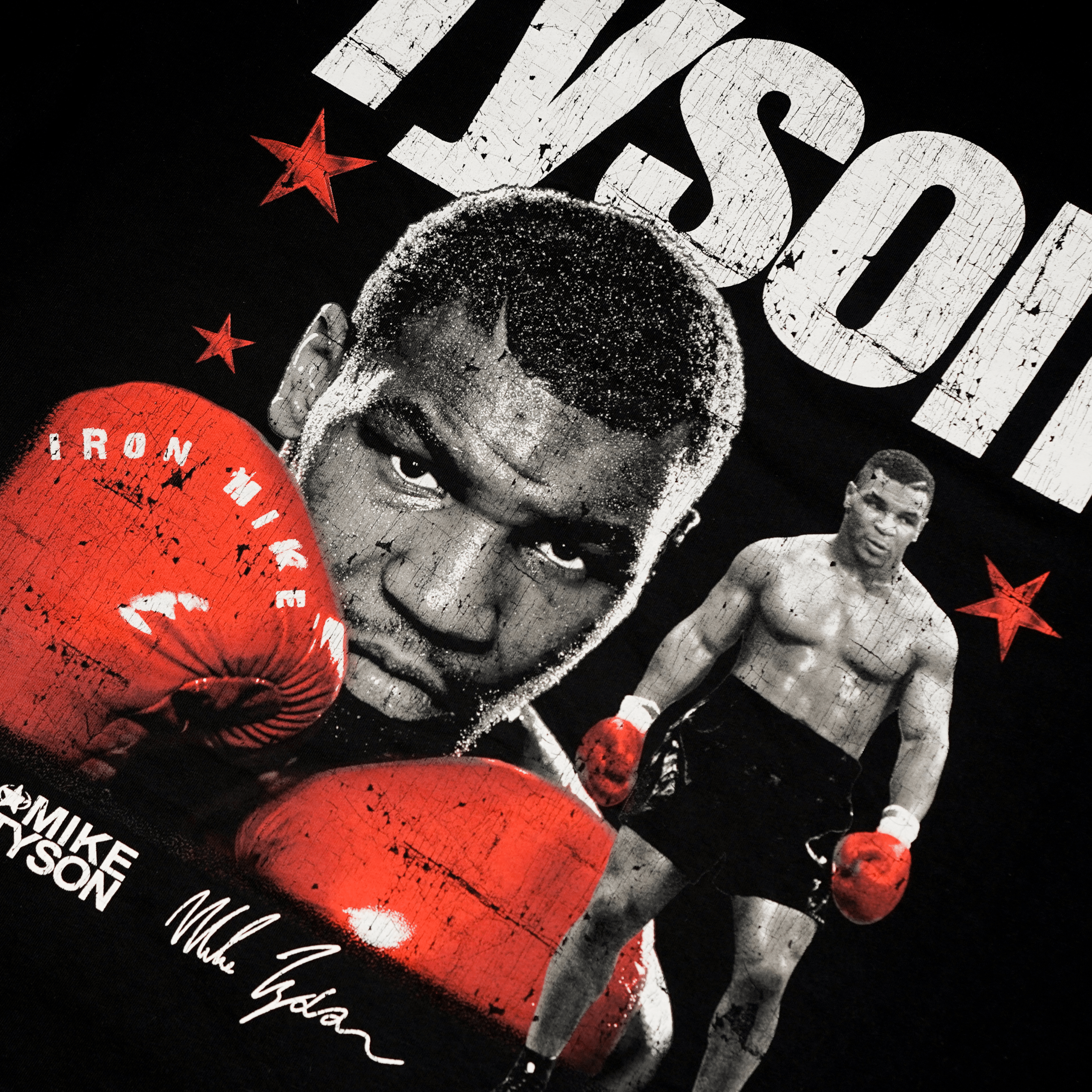Black T-shirt with white text over the left side of the chest that says Tyson. A small Champ emblem, his name Mike Tyson, and his signature are below the Tyson text. The back of the shirt features 2 images of Mike, both showcasing his iconic red gloves. The same text as the front surrounds the image on the back.