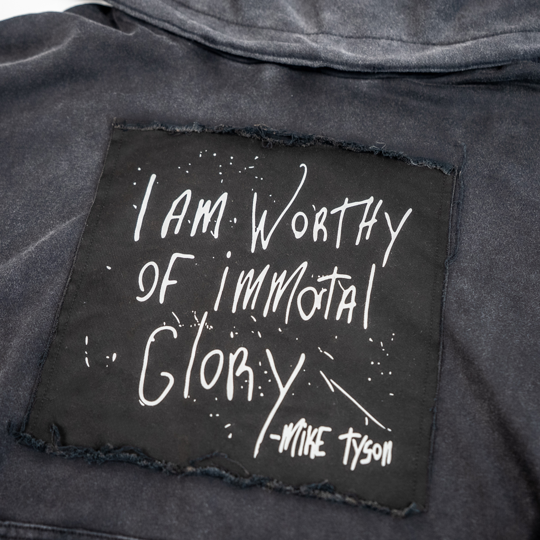 Text on a black patch with 'I am Worthy of Immortal Glory' quote on a black distressed fabric background.