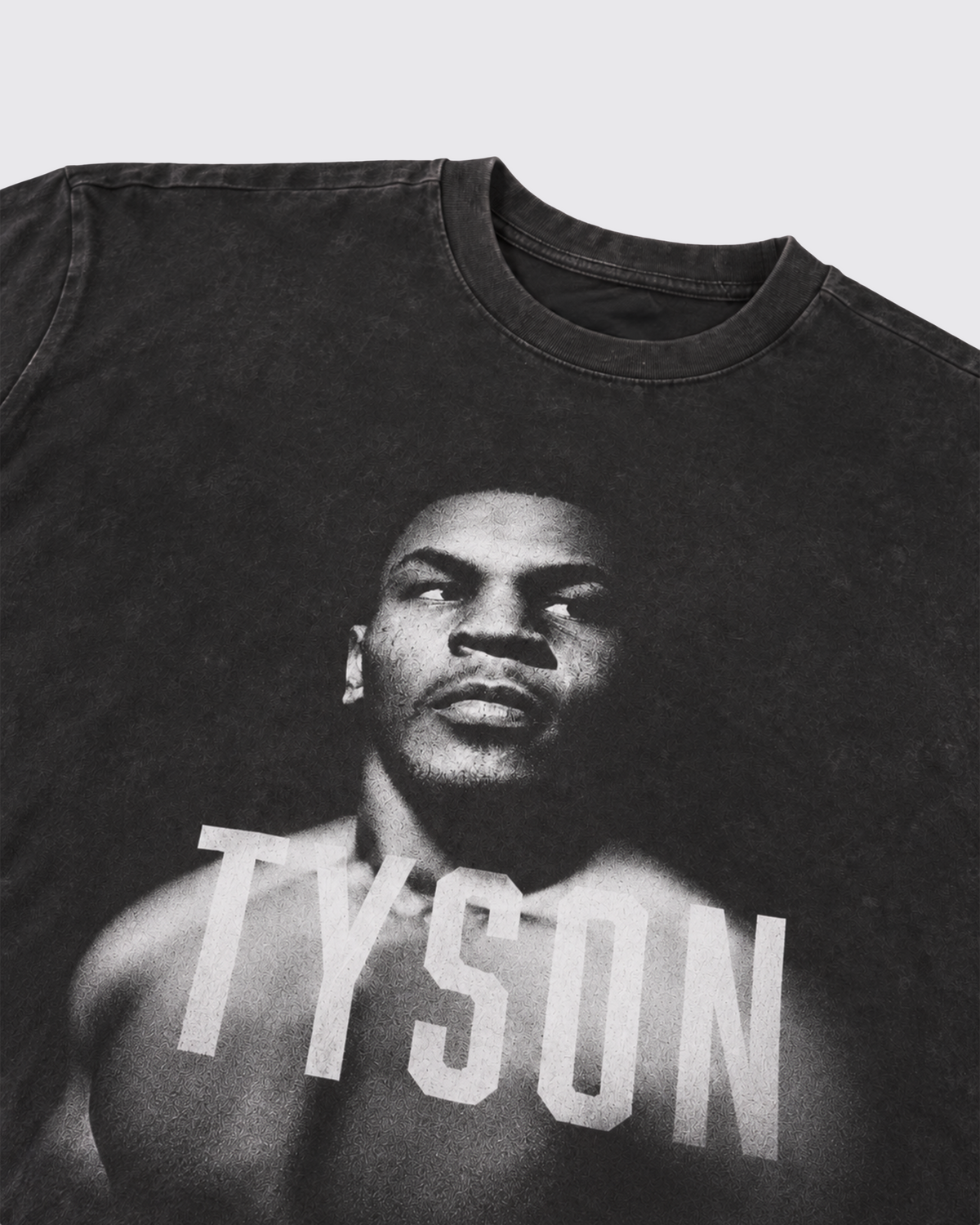 Black, Snow Wash T-shirt with a black and white portrait of Mike. His body is turned slightly to the left, his face is forward and his eyes are looking off to the right. Slightly transparent white text saying "Tyson" is featured across his upper chest. 