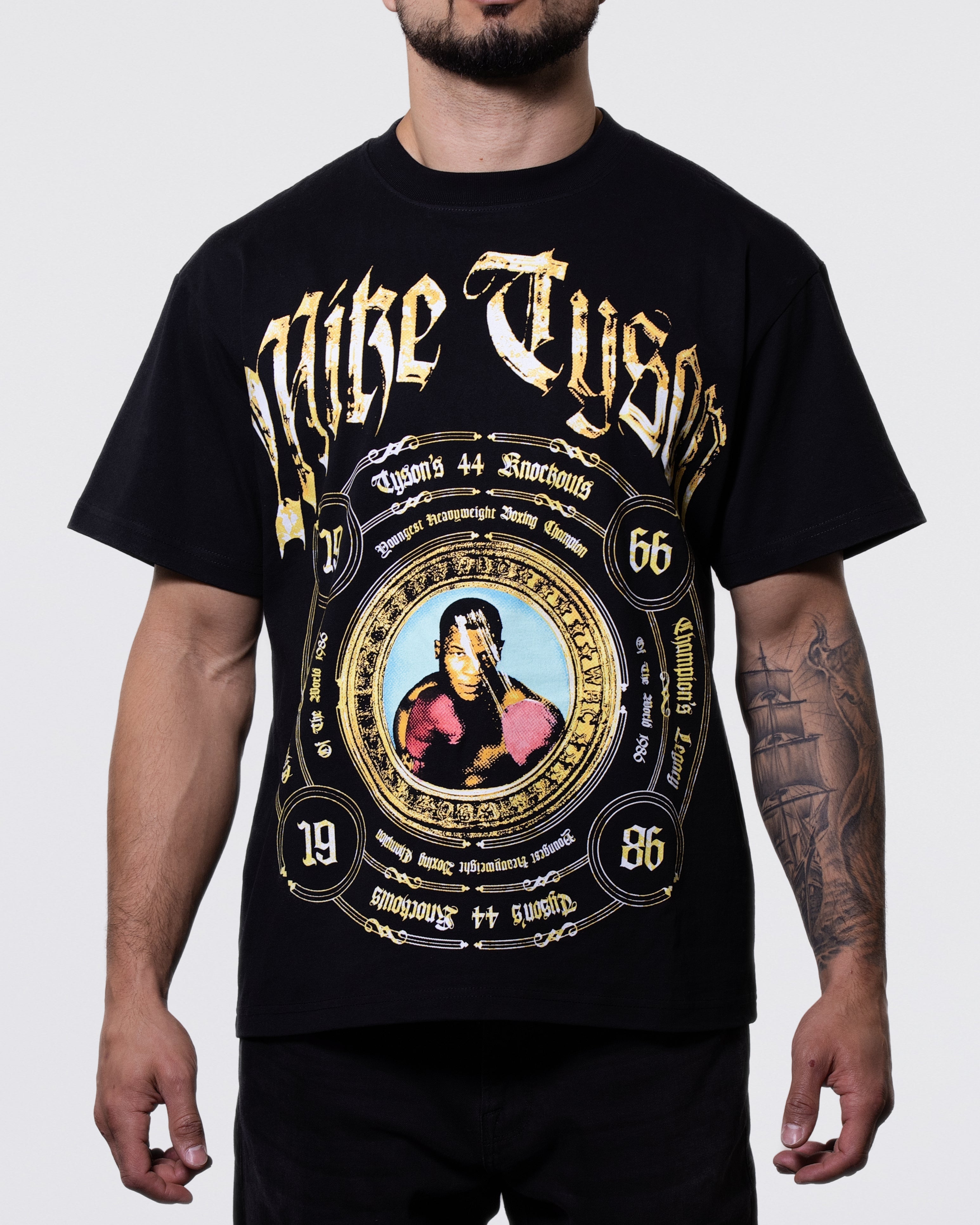 Black T-shirt. The front displays a title belt style design listing some significant dates and achievements from Mike Tyson's career, along with an image of him in the center and his name across the top. The back features the text "Knockout King" and a list of his 44 knockouts.