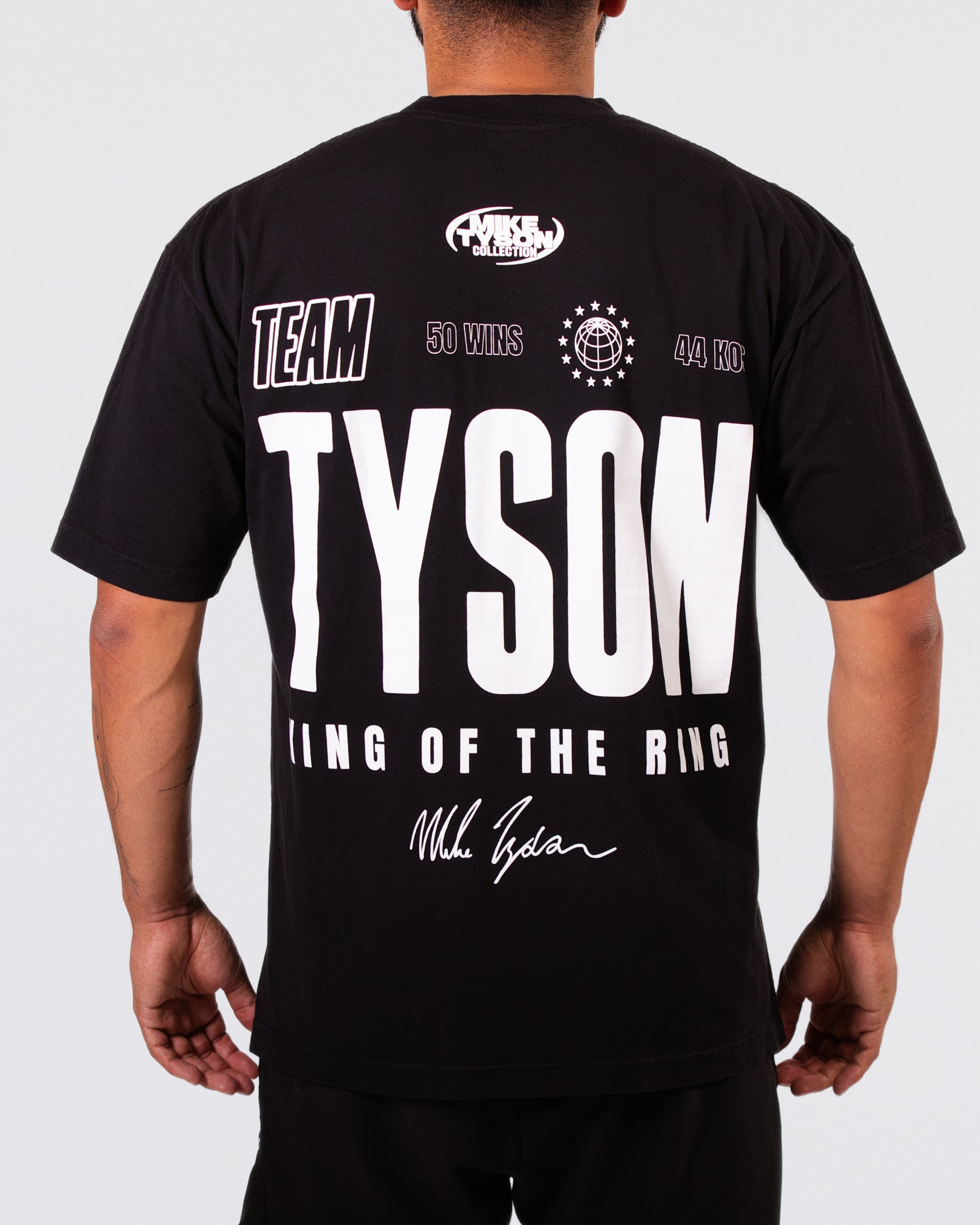 Black T-shirt. The text in front says "Team Tyson. WBC, IBF, WBA Champion. MMXXIV" along with Mike's signature. The back text says "Team Tyson. King of the Ring. 50 Wins, 44 KOS"  with his signature at the bottom.