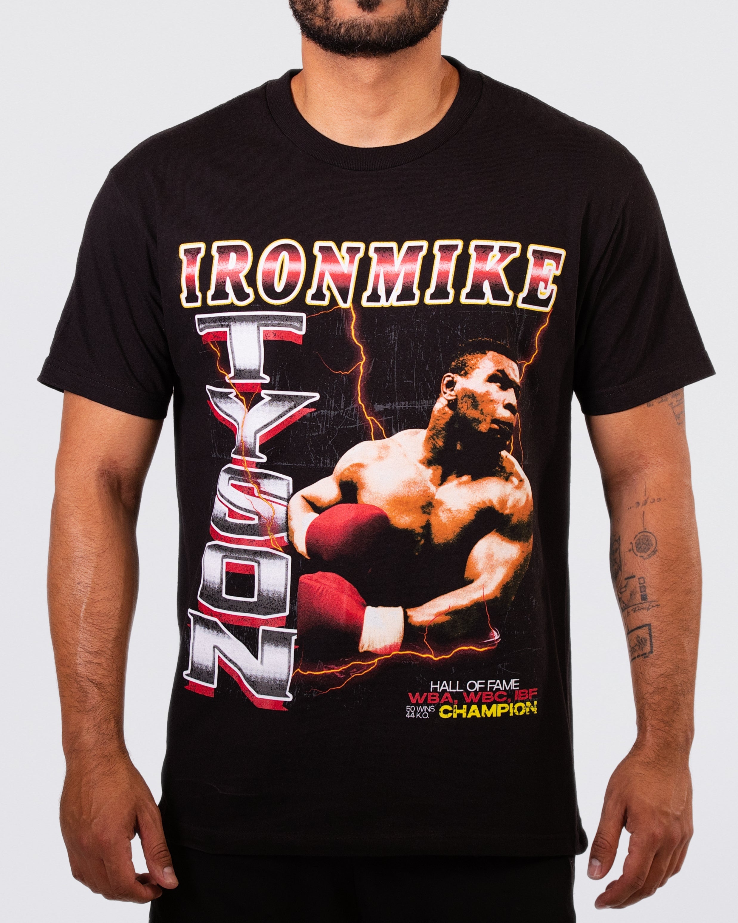 Black T-shirt with an image of Mike mid-punch. "Iron Mike Tyson" text surrounds the image. Small text on the bottom right says "Hall of Fame WBA, WBC, IBF Champion. 50 wins, 44 KO's."