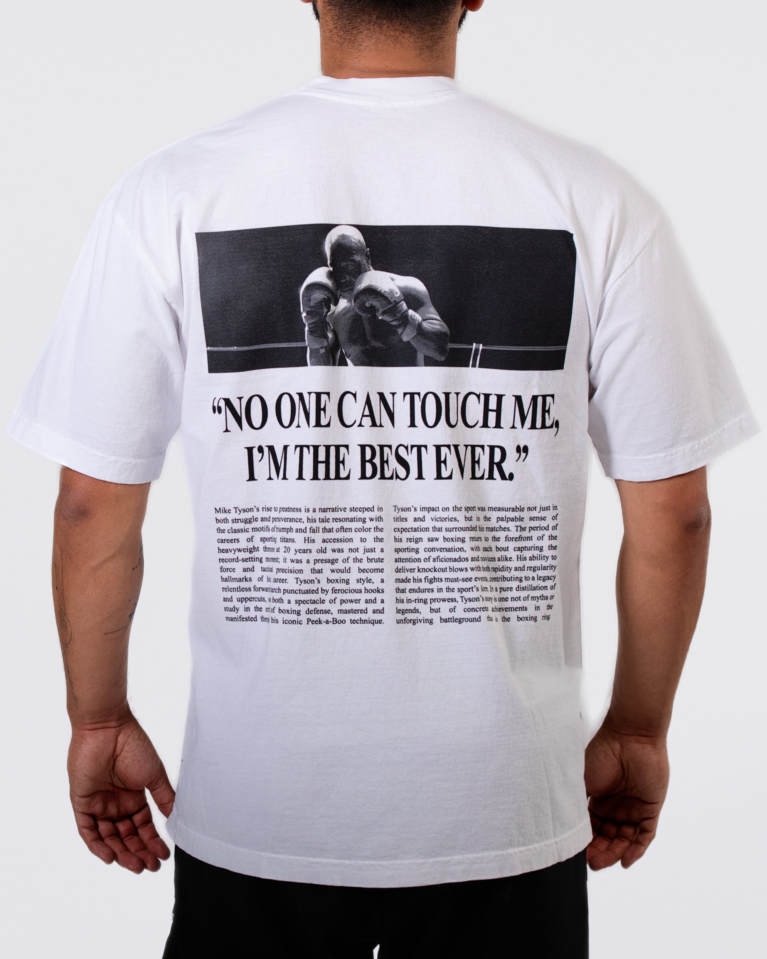 White T-shirt with a graphic on the back in the style of a newspaper article. Across the top, there is a photo of Mike in a ring. Below the image, a large headline reads "No One Can Touch Me, I'm the Best Ever." The article below discusses Mike's road to greatness.