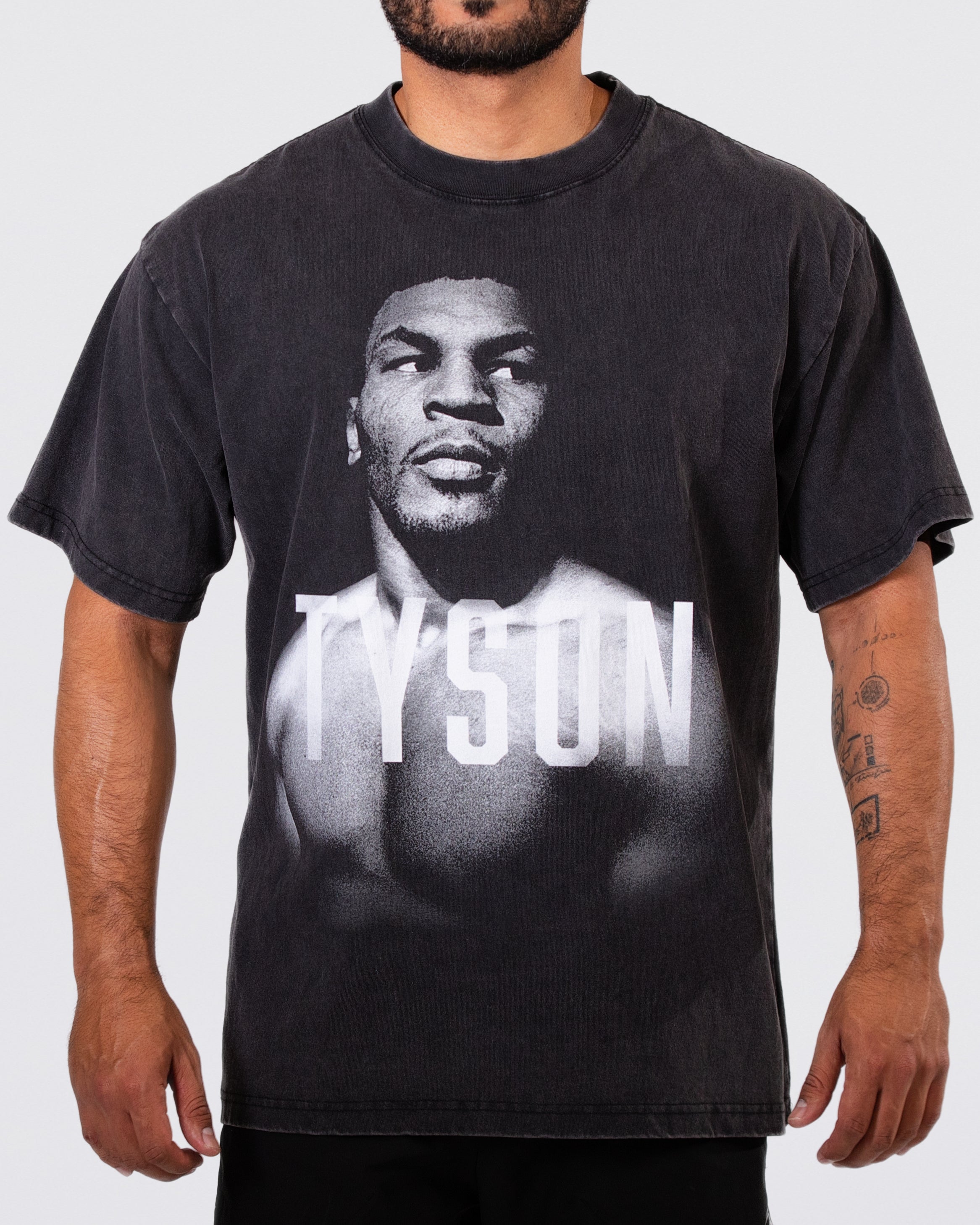 Black, Snow Wash T-shirt with a black and white portrait of Mike. His body is turned slightly to the left, his face is forward and his eyes are looking off to the right. Slightly transparent white text saying "Tyson" is featured across his upper chest. 