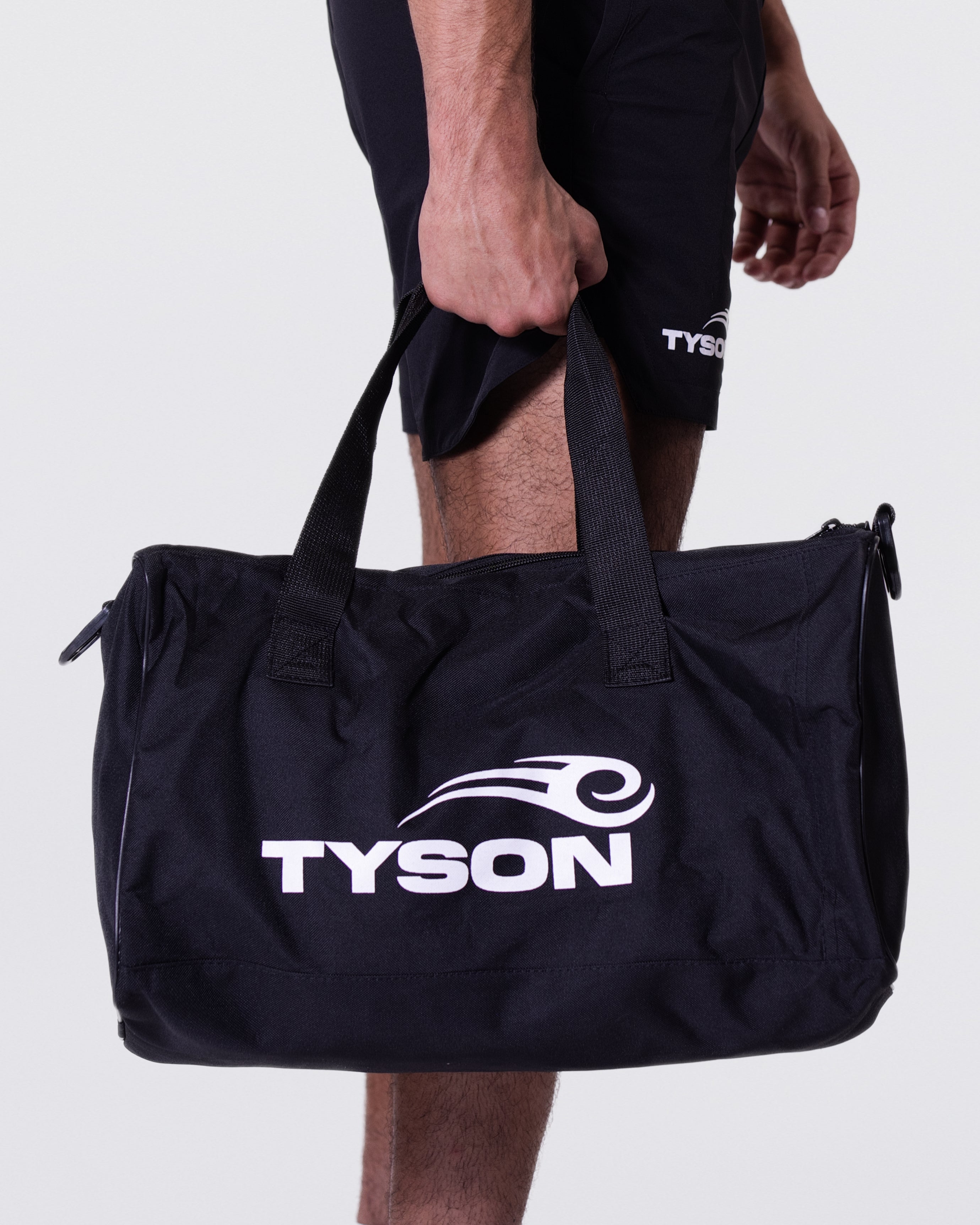 Black rectangular gym bag. The outer face has the white Tyson Pro logo on the bottom right and a mesh pocket to the left. The bag has a shoulder strap and handles.