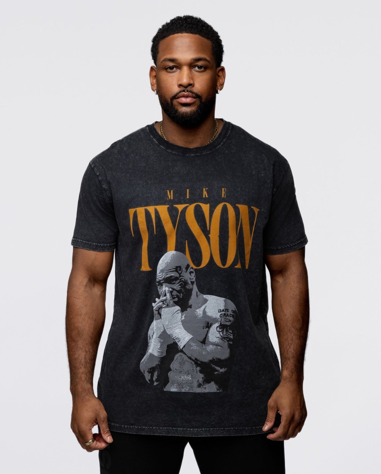 This black shirt features the text "Tyson" in a burnt orange with a pensive Mike Tyson below with his hands folded interlocking into one another. 