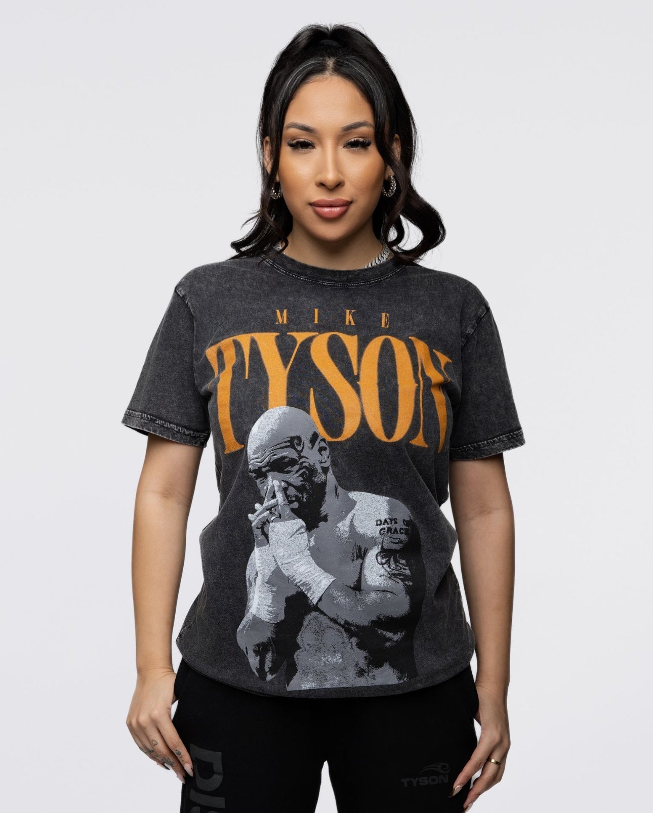 This black shirt features the text "Tyson" in a burnt orange with a pensive Mike Tyson below with his hands folded interlocking into one another.