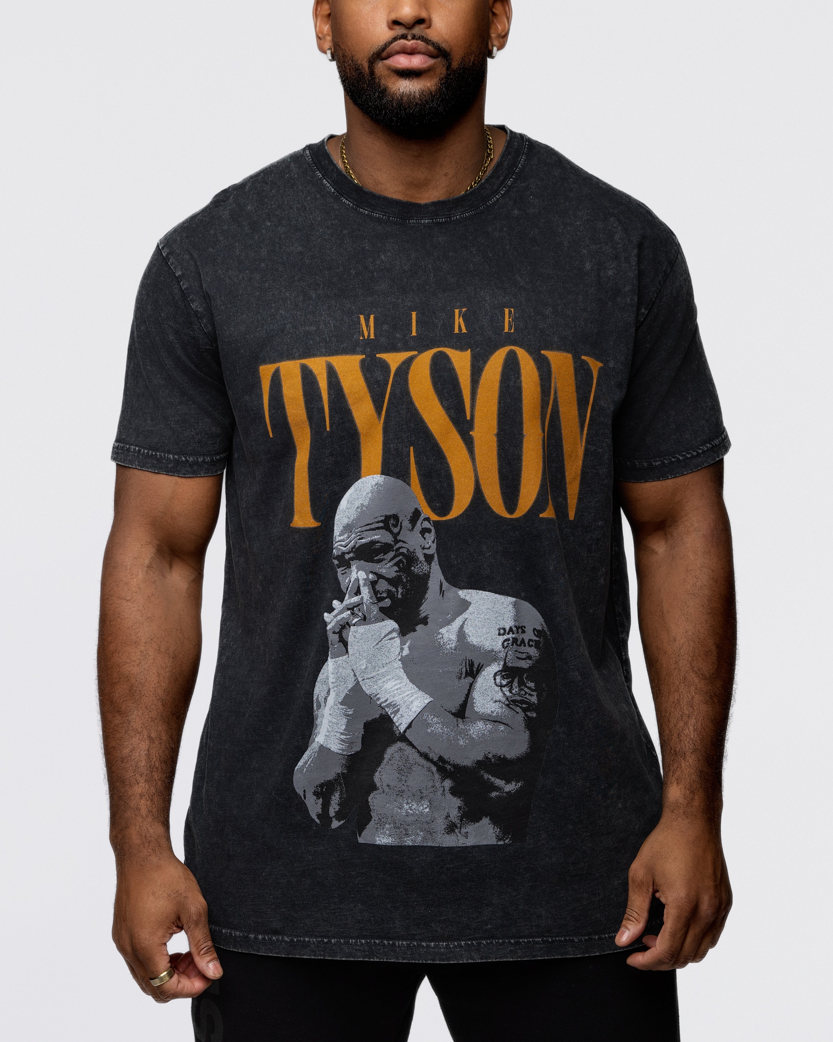 This black shirt features the text "Tyson" in a burnt orange with a pensive Mike Tyson below with his hands folded interlocking into one another.